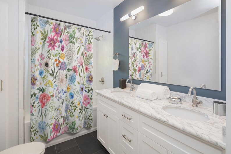 May include: A white bathroom with a floral shower curtain, a white vanity with two sinks, and a large mirror above the sinks.
