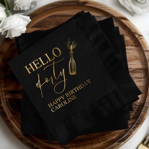 Può includere: Tovaglioli neri con stampa in oro. Il testo recita "Hello Forty" con una grafica di bottiglia di champagne e "Buon compleanno Caroline".