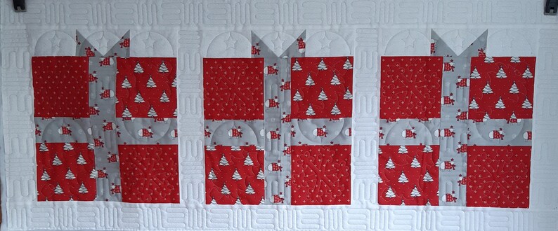 May include: Three red and white gift boxes with a gray ribbon and bow. The boxes are decorated with a white snowflake pattern and a white Christmas tree pattern.
