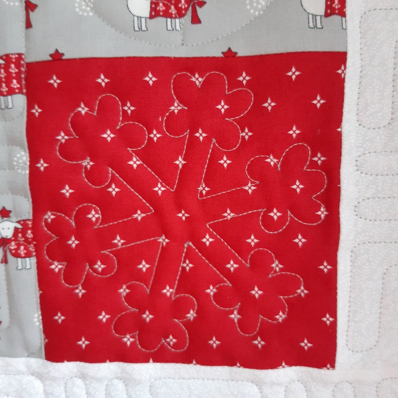 May include: A red fabric square with a white snowflake design quilted on top. The snowflake has six points with rounded edges. The fabric has a white star pattern.