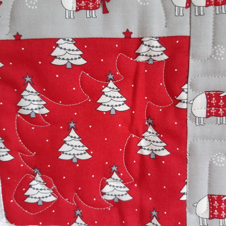 May include: Red fabric with a white background featuring a repeating pattern of white Christmas trees with white lights and a star on top. The fabric is quilted with a white thread in a free-form design.