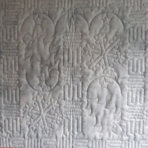 May include: A white quilted fabric with a repeating pattern of snowflakes and crescent moons. The fabric is stitched with a gray thread.