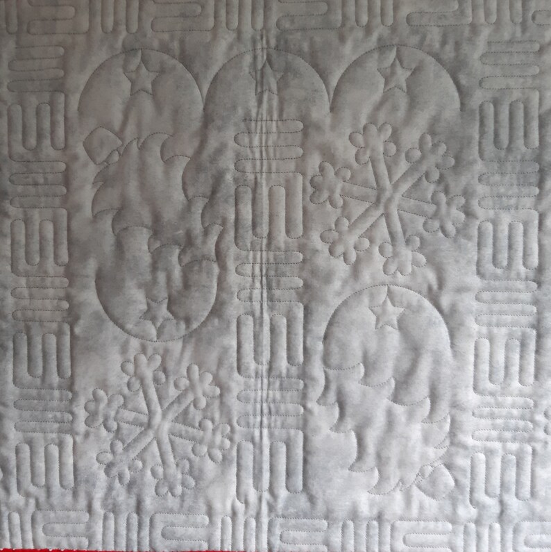 May include: A white quilted fabric with a repeating pattern of snowflakes and crescent moons. The fabric is stitched with a gray thread.
