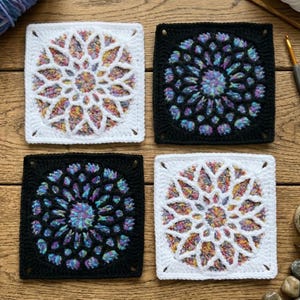May include: Four square crochet motifs featuring a circular mandala pattern. Two squares have a white border with a multicolored center, and two squares have a black border with a multicolored center, all displaying intricate floral-like designs.