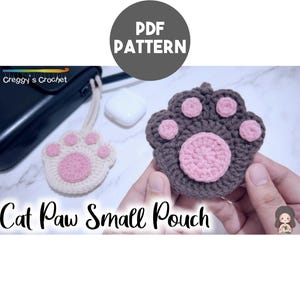 May include: A crochet PDF pattern for a cat paw small pouch. The image displays two finished pouches, one in cream and one in dark brown, both featuring pink circular pads and smaller pink toe pads. The text reads PDF PATTERN and Cat Paw Small Pouch.