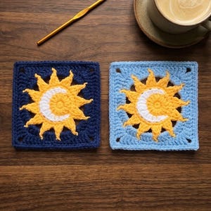 Può includere: Due sottobicchieri quadrati all'uncinetto con un motivo centrale di un sole giallo e una luna crescente bianca. Un sottobicchiere ha uno sfondo blu scuro, mentre l'altro ha uno sfondo azzurro. Un uncinetto dorato è posizionato sopra di essi.