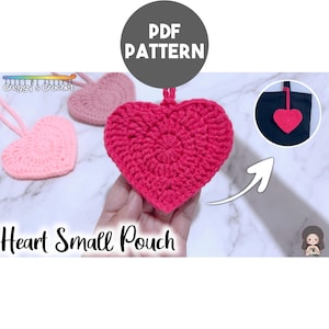 May include: A crochet heart-shaped small pouch in bright pink, with additional light pink and dusty rose heart pouches visible. The image includes the text PDF PATTERN, Creggy's Crochet, and Heart Small Pouch, with an inset showing the pouch on a bag.