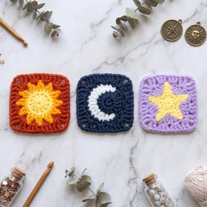 May include: Three square crochet motifs featuring celestial designs. The first is a rust-coloured square with a yellow sun, the second is a navy blue square with a white crescent moon, and the third is a light purple square with a yellow star.