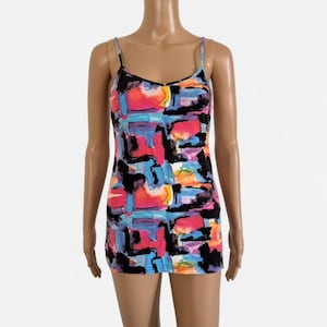 May include: A colorful camisole with thin straps. The top features a vibrant abstract pattern in shades of pink, blue, orange, and black. The garment is displayed on a mannequin.