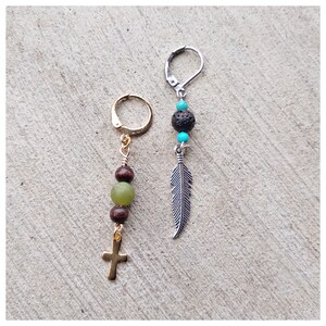 May include: Two pairs of earrings with different charms. One pair has a gold hoop with brown and green beads and a gold cross charm. The other pair has a silver hoop with a turquoise bead, a black lava bead, and a silver feather charm.
