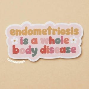 May include: A die-cut sticker with a light pink background featuring the text "endometriosis is a whole body disease" in a multi-coloured, rounded font. The design includes two small white flower icons and the text "TWINTOWNAU" in the corner.