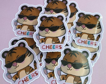 Può includere: Un set di otto adesivi di tigre colorati con occhiali da sole e un bicchiere di champagne. Ogni adesivo dice "Cheers" in un font arcobaleno.