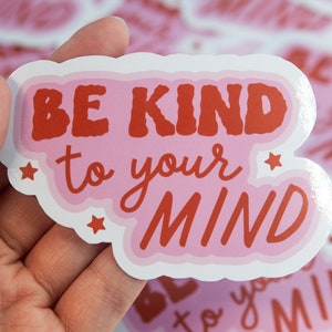 May include: Pink and red sticker with the text "Be Kind to Your Mind" in a retro font. The sticker has a white border and stars around the text.