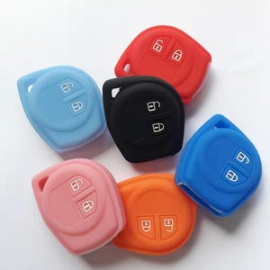 May include: A selection of car key fobs in a range of colours: red, black, blue, pink, and orange. Each fob features a key and lock icon. The fobs are made from a soft, flexible material.
