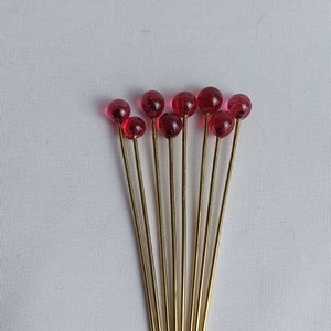 Può includere: Otto stuzzicadenti da cocktail dorati con palline di vetro rosse.