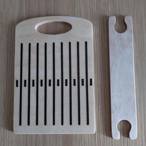 May include: A wooden loom with a handle and 12 slots for weaving. The loom is made of light wood and has a dark brown stain. It comes with a separate wooden shuttle.