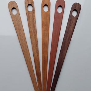 Può includere: Cinque ferri da maglia in legno con un foro nella parte superiore. I ferri sono di diverse tonalità di marrone, rosso e marrone scuro.