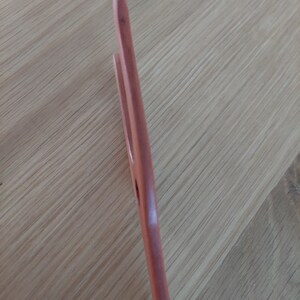 May include: A wooden kitchen utensil, possibly a pair of tongs or a spatula, with a light brown color. The utensil has a smooth, polished finish and a simple, functional design. The image is taken at an angle, showing the side profile of the utensil.