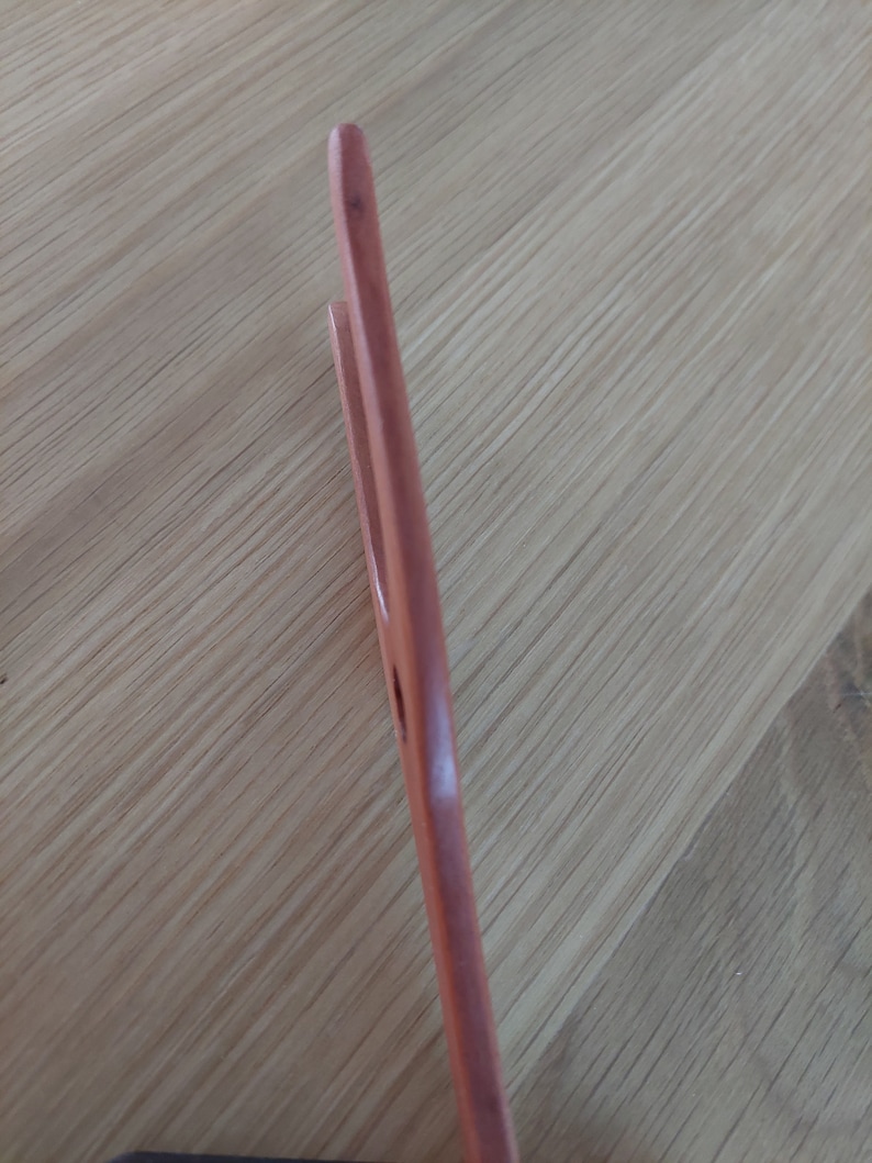 May include: A wooden kitchen utensil, possibly a pair of tongs or a spatula, with a light brown color. The utensil has a smooth, polished finish and a simple, functional design. The image is taken at an angle, showing the side profile of the utensil.