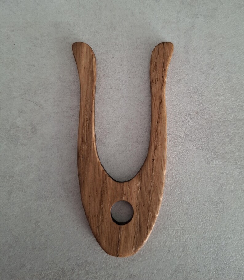 May include: A wooden hair fork with a U-shaped design. The fork is made of light brown wood with a visible grain pattern. It has a rounded hole near the base and curved tines. The hair accessory is designed for styling and securing hair.