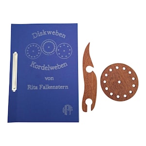 Op de afbeelding: Een blauwe map met een metalen klem, voorzien van de tekst Diskweben Kordelweben von Rita Falkenstern en een logo. Daarnaast liggen een gebogen houten gereedschap en een ronde houten schijf met meerdere gaatjes in een patroon.