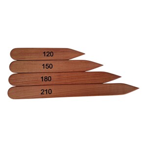 May include: Four wooden plant markers with pointed ends, each displaying a different number: 120, 150, 180, and 210. The markers are a warm brown colour and appear to be made of wood. These are ideal for organising a garden.
