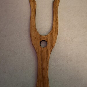 May include: A wooden hair tool with a U-shaped top and a circular hole in the center. The tool is made of light brown wood with a visible wood grain pattern. The handle is smooth and rounded.