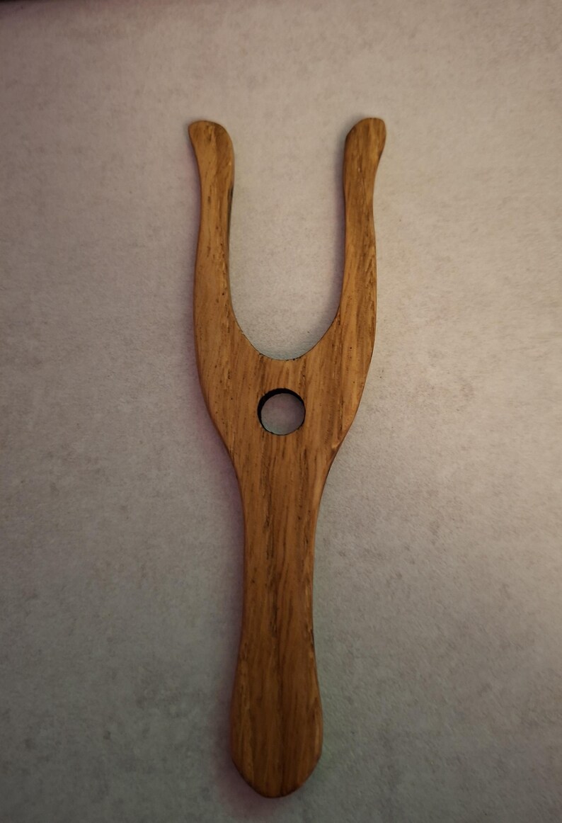 May include: A wooden hair tool with a U-shaped top and a circular hole in the center. The tool is made of light brown wood with a visible wood grain pattern. The handle is smooth and rounded.