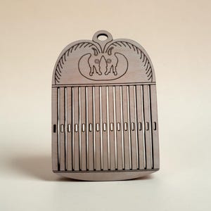 Peut inclure: Un outil de tissage en bois brun clair avec un sommet arrondi et un trou circulaire pour la suspension. La surface présente un motif gravé de deux figures animales symétriques au-dessus d'une série de fentes verticales et de petites découpes.