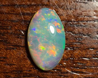 May include: A light gray oval opal gemstone with flashes of green, blue, orange, and red.