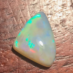 May include: A triangular, white opal gemstone with green and blue iridescence.