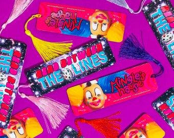 May include: A collection of colorful bookmarks with various designs. Some feature a clown face with the text "Mingle's House", while others have a space background with the text "Read Between The Lines".