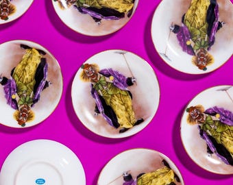 May include: Nine white porcelain plates with gold trim, each featuring a colorful illustration of a clown juggling. The plates are arranged in a grid pattern on a bright pink background.