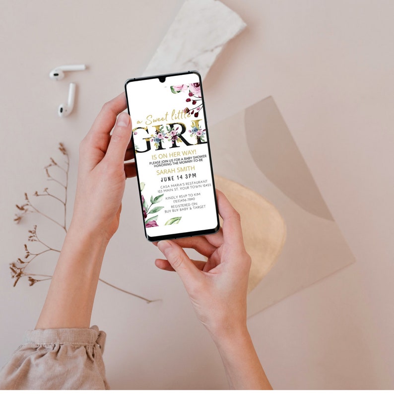 May include: A digital invitation for a baby shower with a floral design and gold lettering. The text reads "a Sweet little GIRL is on her way!" and includes the date, time, and location of the event. RSVP information and registry details are also included.