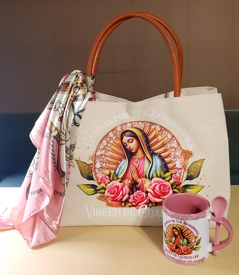 Puede incluir: Una bolsa de lona blanca con asas de cuero marr&oacute;n. La bolsa presenta una imagen colorida de la Virgen de Guadalupe con el texto "Gracias por tus bendiciones Virgen de Guadalupe". Una taza de cer&aacute;mica rosa con una cuchara y una imagen similar de la Virgen de Guadalupe est&aacute; en primer plano.