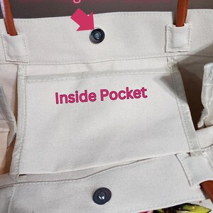 Puede incluir: Una bolsa de lona blanca con asa de cuero marr&oacute;n. La bolsa tiene un cierre magn&eacute;tico y un bolsillo interior. El texto "Inside Pocket" est&aacute; impreso en el bolsillo.