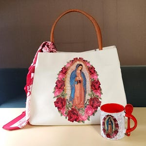 Puede incluir: Bolsa de tela blanca con asa marr&oacute;n y una imagen impresa de la Virgen Mar&iacute;a rodeada de rosas rojas. Una taza roja con una imagen similar est&aacute; al lado de la bolsa.
