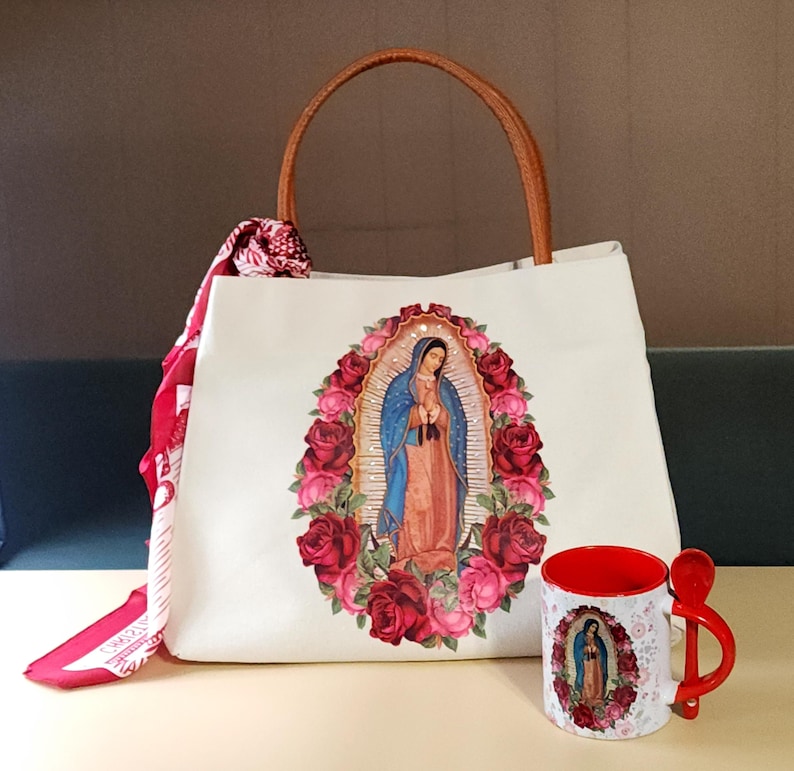 Puede incluir: Bolsa de tela blanca con asa marr&oacute;n y una imagen impresa de la Virgen Mar&iacute;a rodeada de rosas rojas. Una taza roja con una imagen similar est&aacute; al lado de la bolsa.