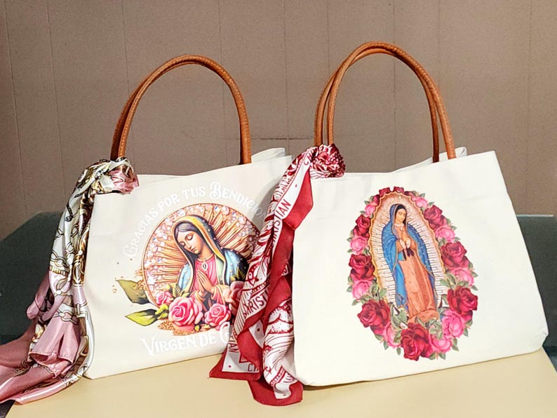 Puede incluir: Dos bolsas de lona blancas con asas de cuero marr&oacute;n. Una bolsa presenta una imagen colorida de la Virgen Mar&iacute;a con rosas. La otra bolsa presenta una imagen colorida de la Virgen Mar&iacute;a con rosas y el texto "Gracias por tus Bendiciones Virgen de Guadalupe".