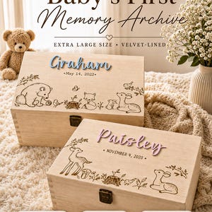 May include: Two rectangular light-colored wooden keepsake boxes with metal latches. The top box features the name Graham in blue and May 14, 2022, with woodland animal engravings. The bottom box features the name Paisley in pink and November 4, 2020.