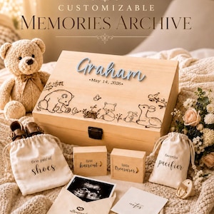 May include: A wooden memory box with the name Graham and May 14, 2026 engraved, featuring forest animal illustrations. Includes two fabric drawstring bags labeled first pair of shoes and favorite pacifier, two small wooden boxes, and an ultrasound photo.