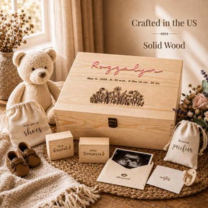 May include: A wooden keepsake box engraved with the name Rozzalyn, birth details, and floral art. Includes a teddy bear, two small wooden blocks labeled first haircut and little treasures, two fabric pouches, an ultrasound photo, and a pacifier.