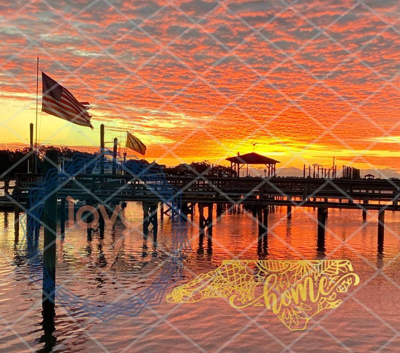 Puede incluir: Una puesta de sol pintoresca sobre un muelle de madera con una silueta de un cenador y una bandera estadounidense ondeando en la brisa. El agua refleja los tonos naranja y rosa del cielo. Las palabras "home" y "love" est&aacute;n superpuestas a la imagen.
