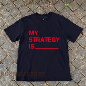 May include: Black t-shirt with the text "MY STRATEGY IS" in red.