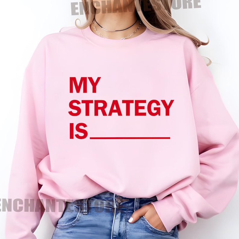 May include: Pink sweatshirt with the text "MY STRATEGY IS" in red.