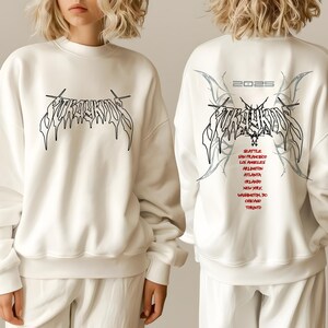 May include: White sweatshirt with a black graphic print of the word "FOREVER" in a gothic font. The back of the sweatshirt has the same graphic with the year "2025" and a list of cities in red text.