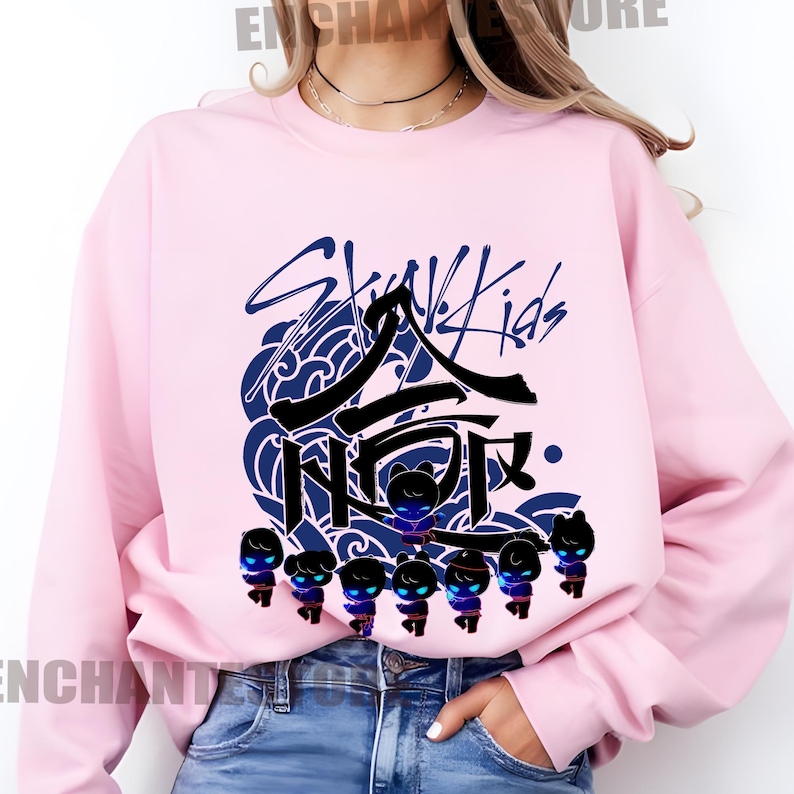 Może przedstawiać: R&oacute;żowa bluza z czarno-niebieskim nadrukiem koreańskiego boysbandu Stray Kids. Nadruk zawiera nazwę zespołu, stylizowany wz&oacute;r fali i grupę postaci z kresk&oacute;wek.