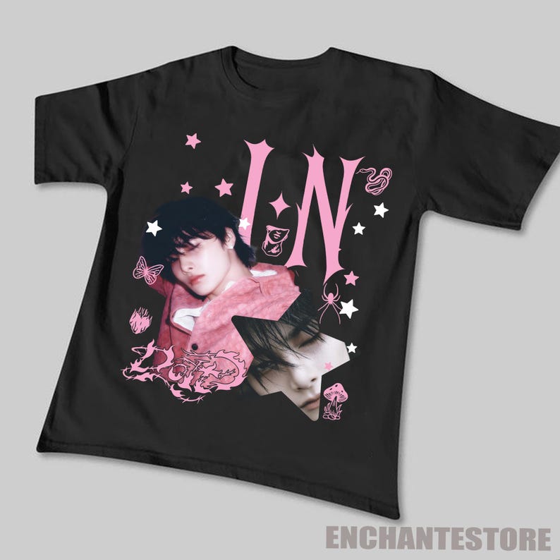 Pu&ograve; includere: T-shirt nera con un design grafico rosa. Il design include le lettere "IN", una foto di una persona, stelle, una farfalla, un ragno e un fungo. Il testo "ENCHANTESTORE" &egrave; in basso.