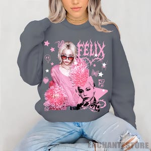 Pu&ograve; includere: Felpa grigia con grafica rosa raffigurante una persona con occhiali da sole e il nome "FELIX" in rosa. Il design include stelle, farfalle e altri elementi decorativi. Fa parte di una collezione di abbigliamento.