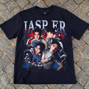 May include: Black t-shirt featuring the word "JASPER" in a blue and silver font. The shirt has a graphic of four people in various poses. The background has red and blue accents.